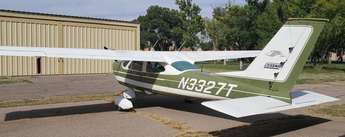 A Cessna aircraft with a green and white paint scheme is parked near a hangar.