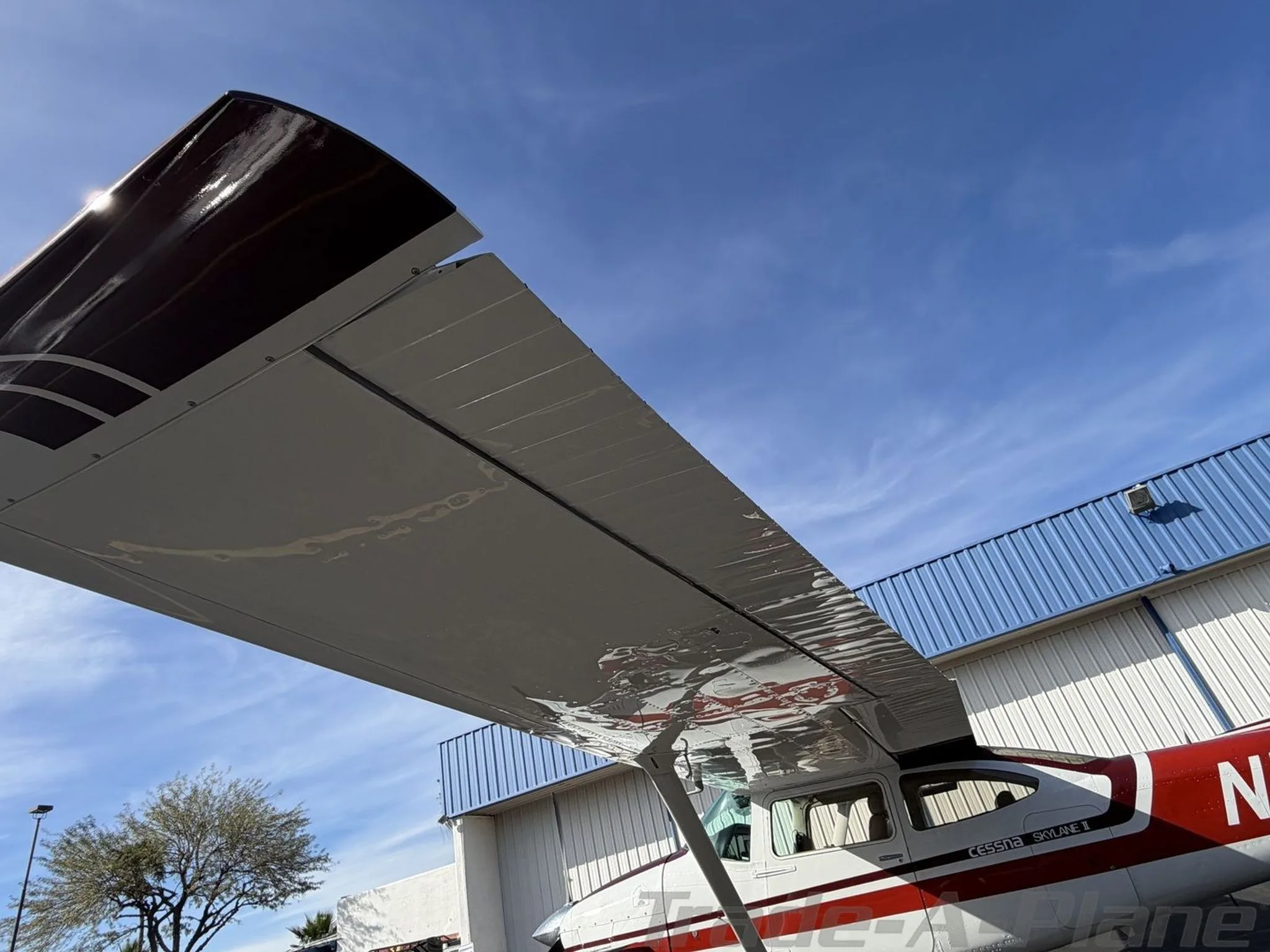 An upward view of the underside of the right wing and fuselage of the white and red Cessna Skylane II (N1475S).