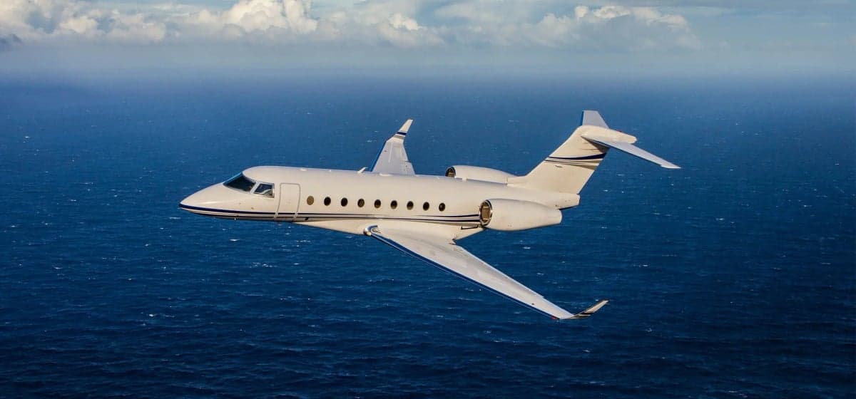 A white Gulfstream jet flies over the ocean.