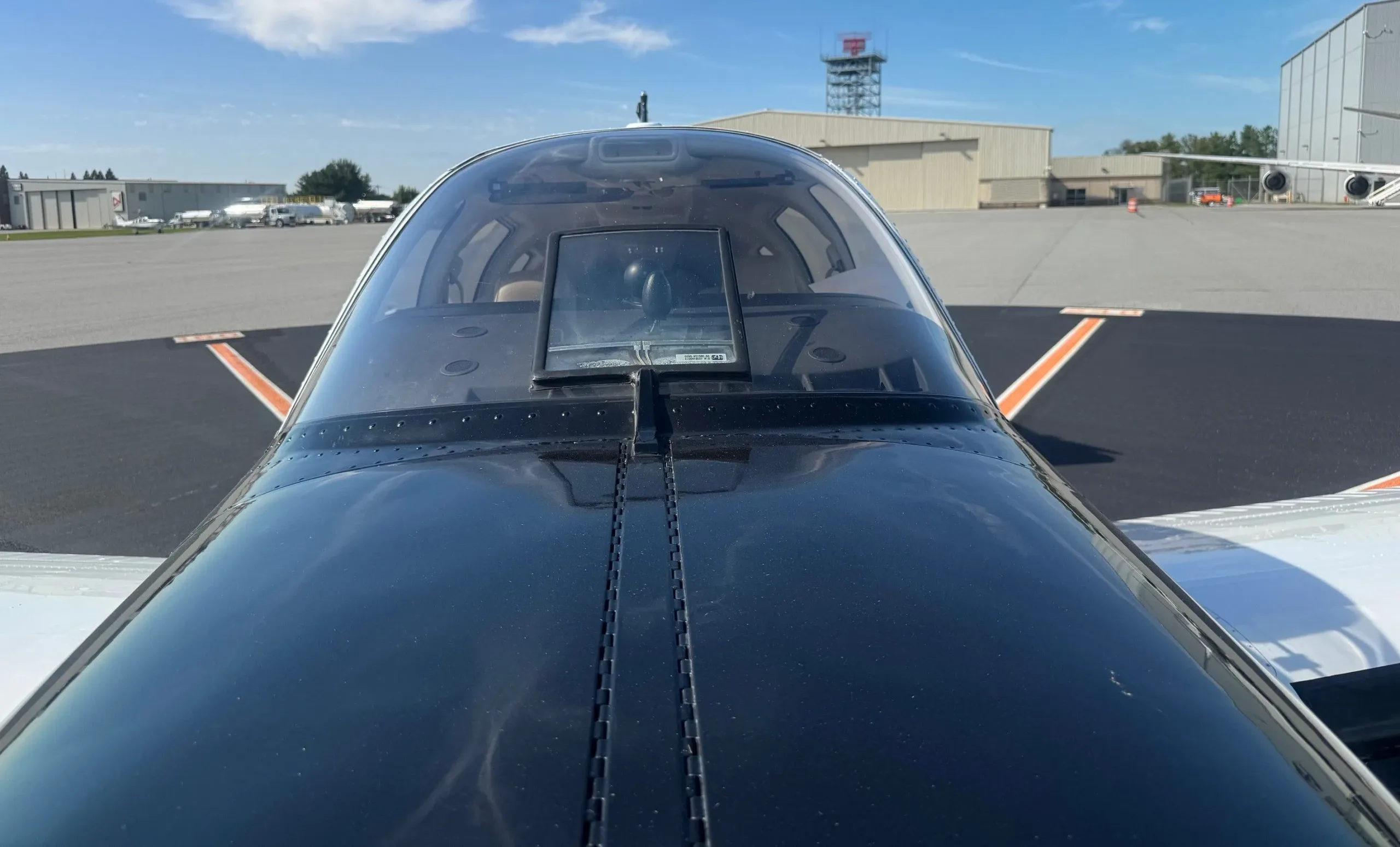 An overhead view looking forward from the tail of the black and white Beechcraft Bonanza towards the cockpit and runway.