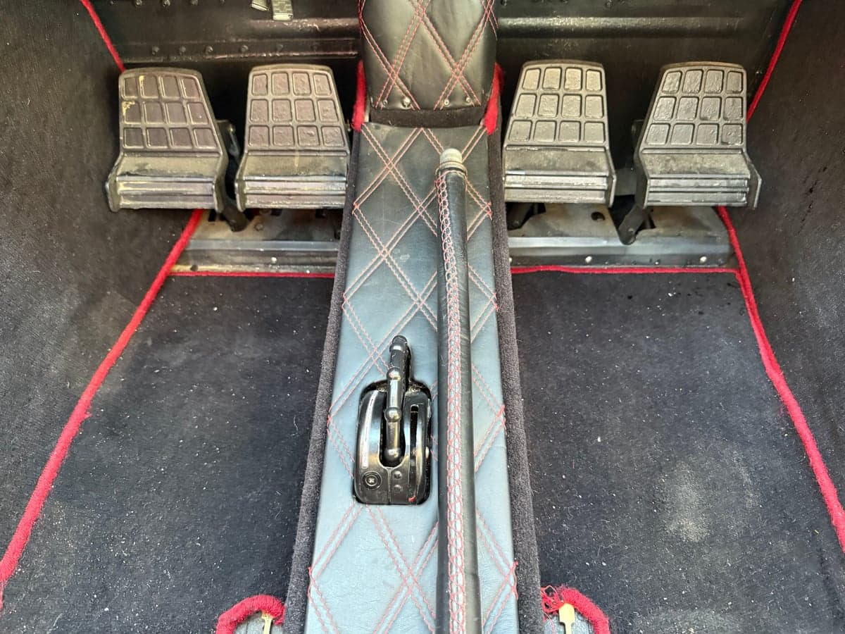 View of the aircraft's rudder pedals and control stick, with black carpet and red trim.