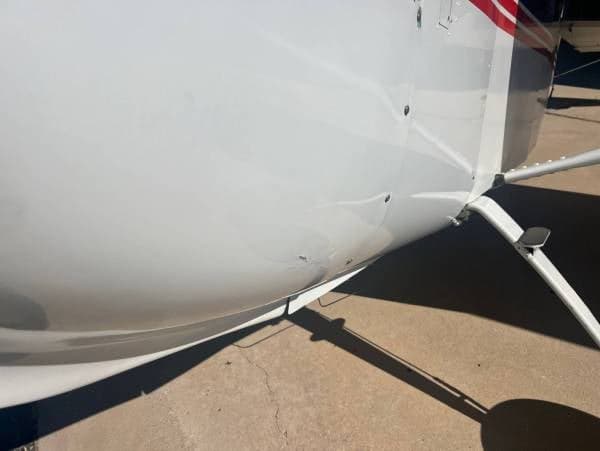 A close-up view of the white fuselage of the aircraft, showing some minor dents and the landing gear strut.