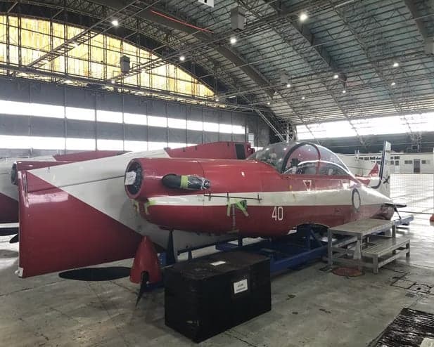 Side view of a red and white Pilatus PC-9 aircraft in a hangar.
