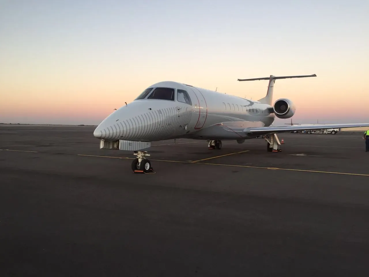 A white Embraer Legacy 600 business jet is parked on the tarmac at sunset.