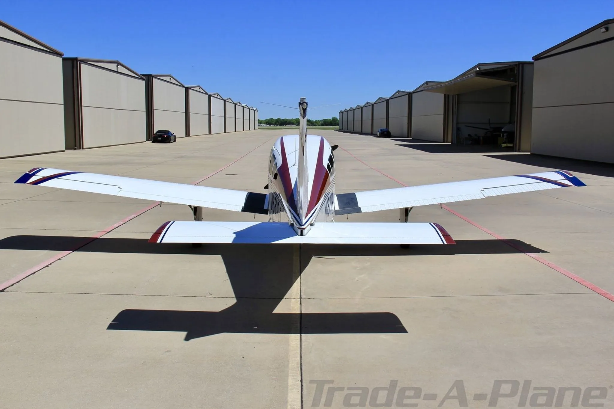 A rear view of the white, blue, and red single-engine aircraft N66304, parked on an apron between hangars.