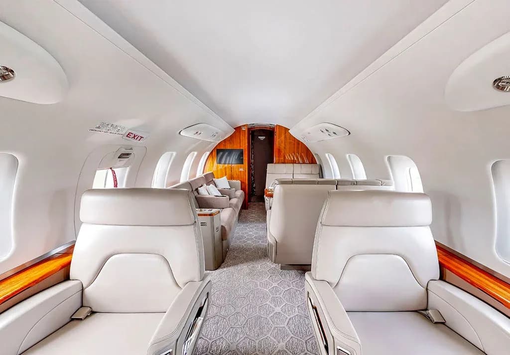 The luxurious interior of a private jet cabin with light-colored seats and a rear lounge area.