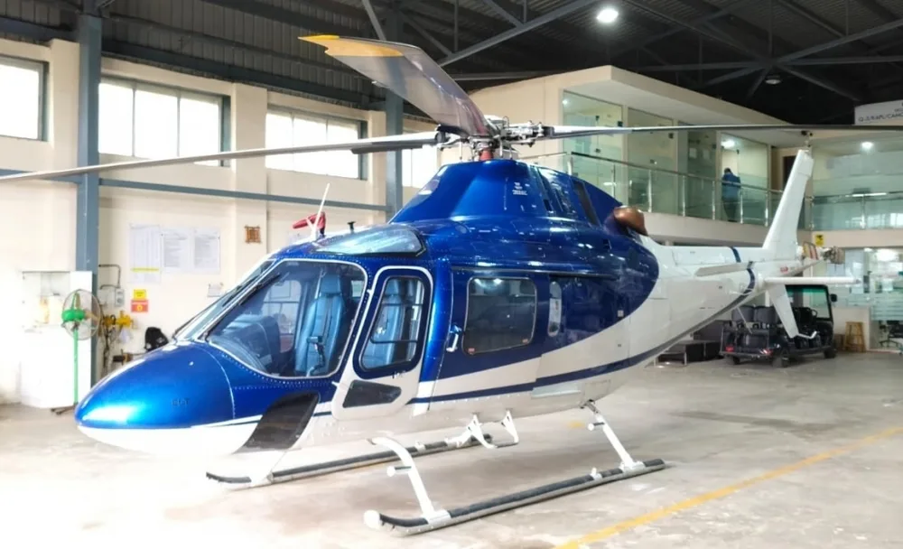 A blue and white helicopter with its main rotor blades extended, parked inside a hangar.