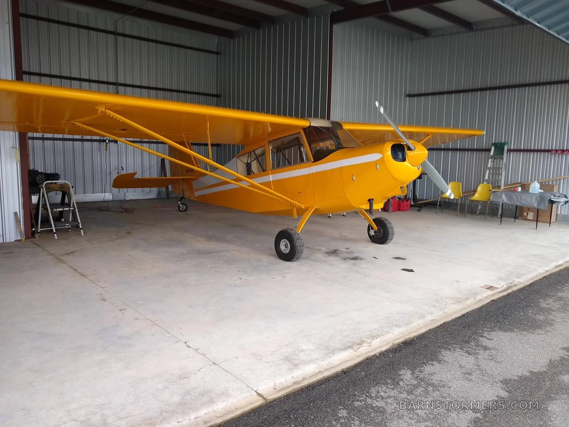 A yellow high-wing aircraft with white stripes parked inside a metal hangar.