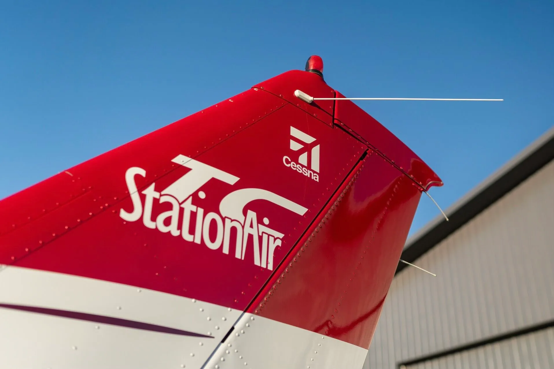 A close-up of the red tail of a Cessna StationAir aircraft, featuring white "StationAir" and "Cessna" logos.