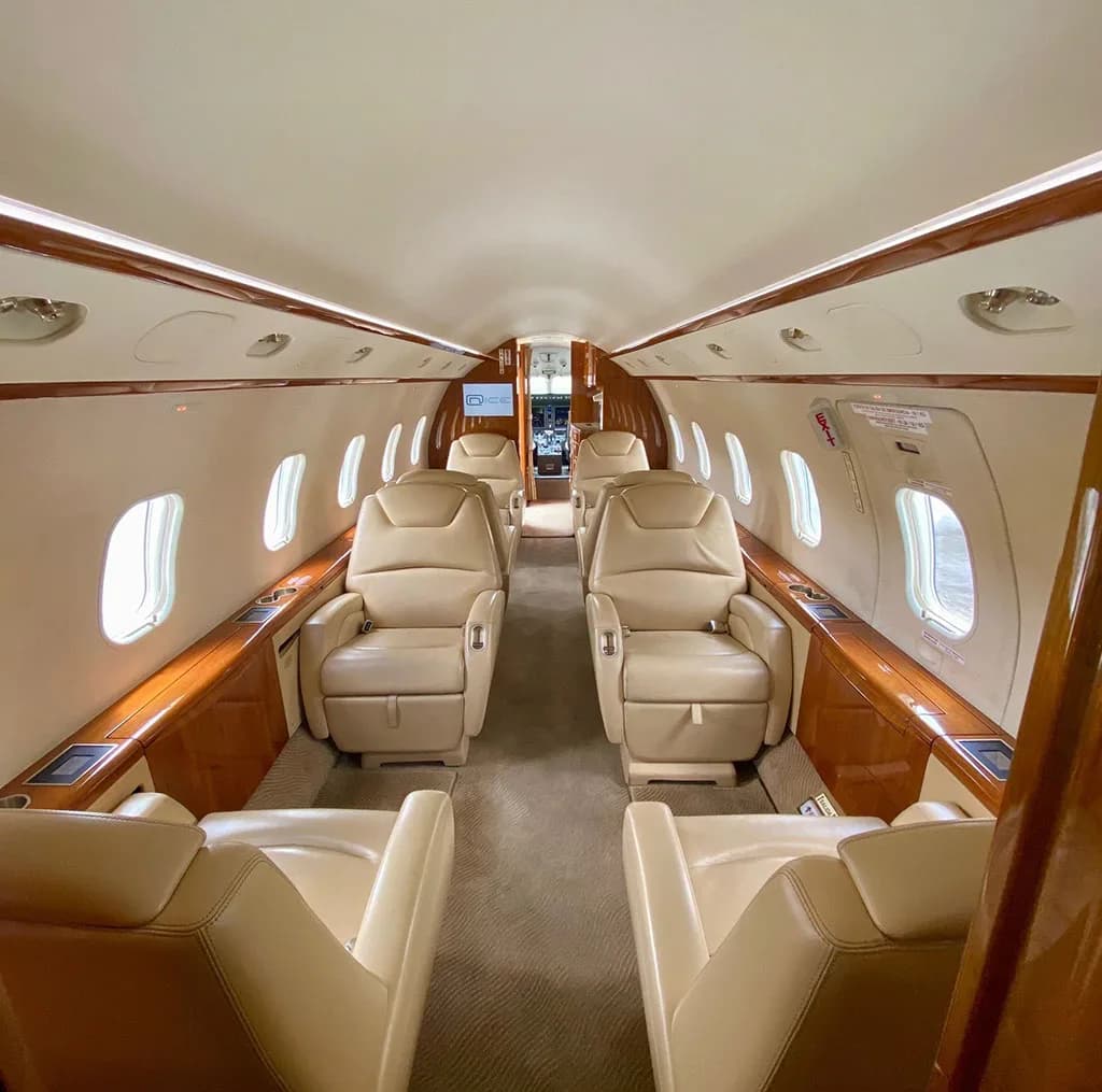 The luxurious interior of a private jet cabin features rows of beige leather seats and polished wood accents.