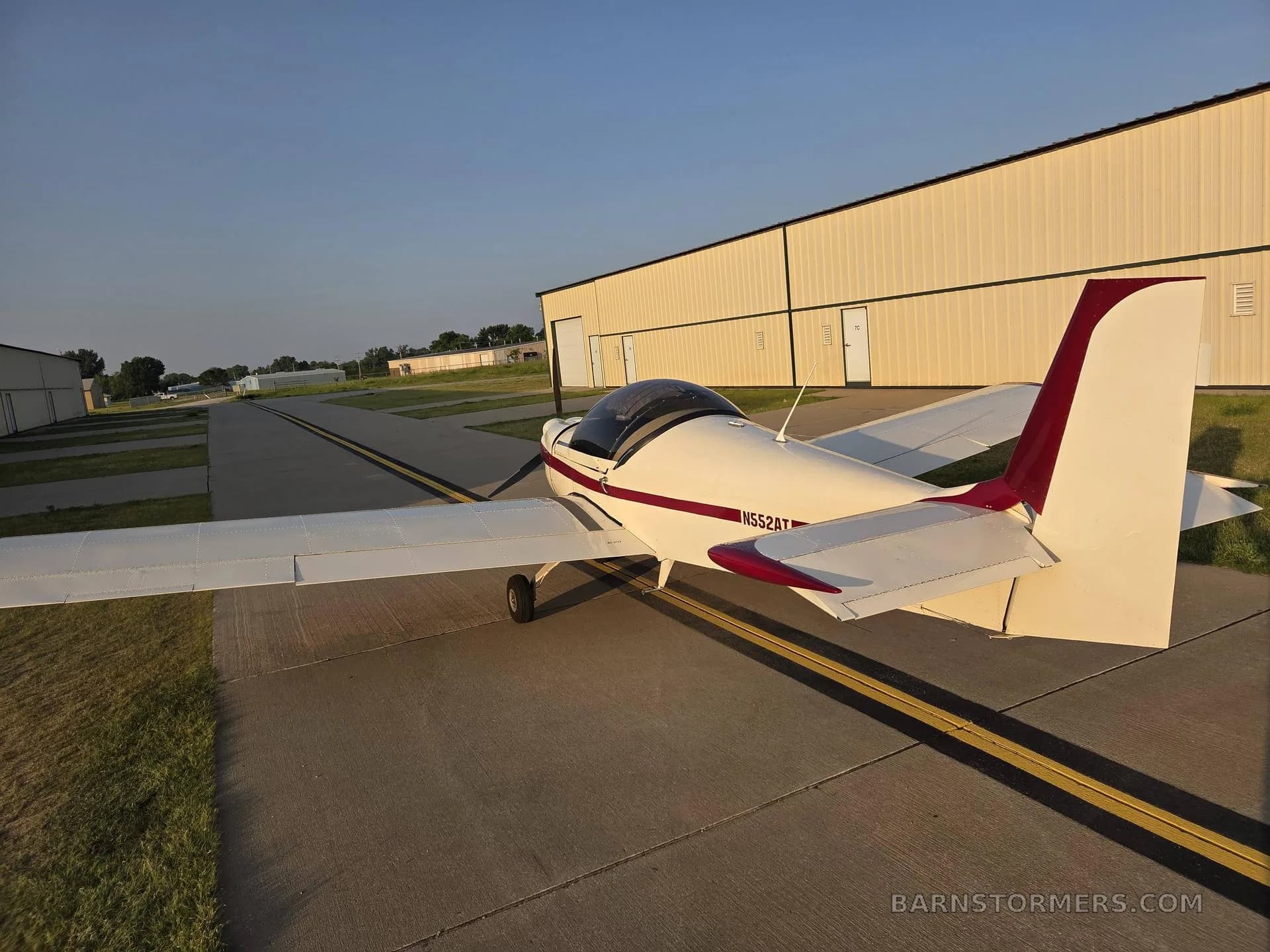 A white and red single-engine aircraft with tail number N552AT is viewed from the rear on an airport taxiway.