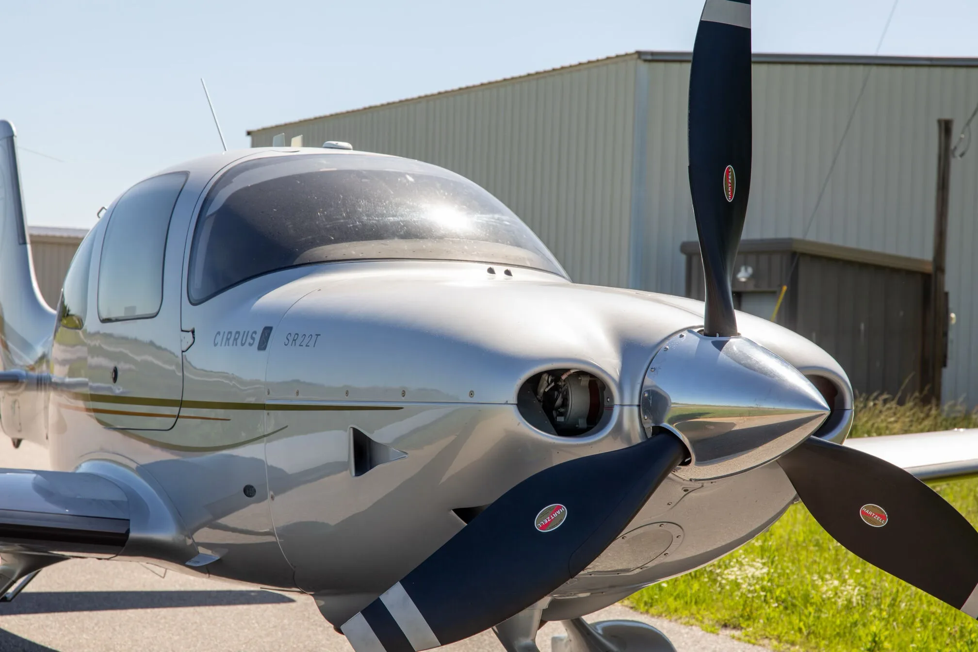 A close-up view of the nose and three-bladed propeller of the silver Cirrus SR22T aircraft.