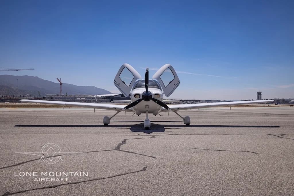 A white Cirrus aircraft with registration N878EA and open doors is viewed head-on while parked on an airfield.
