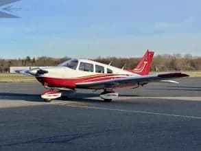 A Piper PA-28 Cherokee with a white and red paint scheme parked on the tarmac.