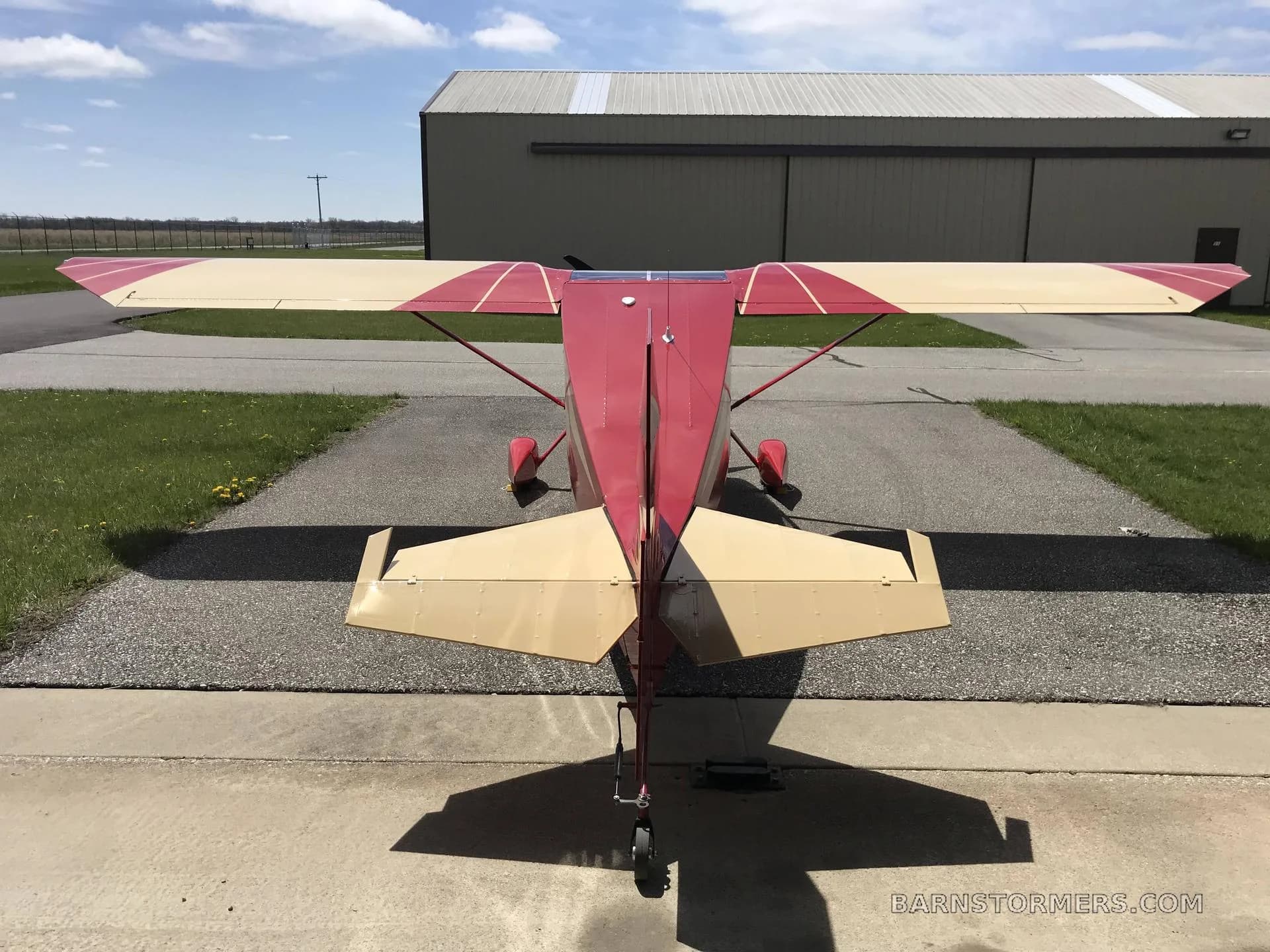 A rear view of a red and cream single-engine aircraft with floats, parked on an airfield.