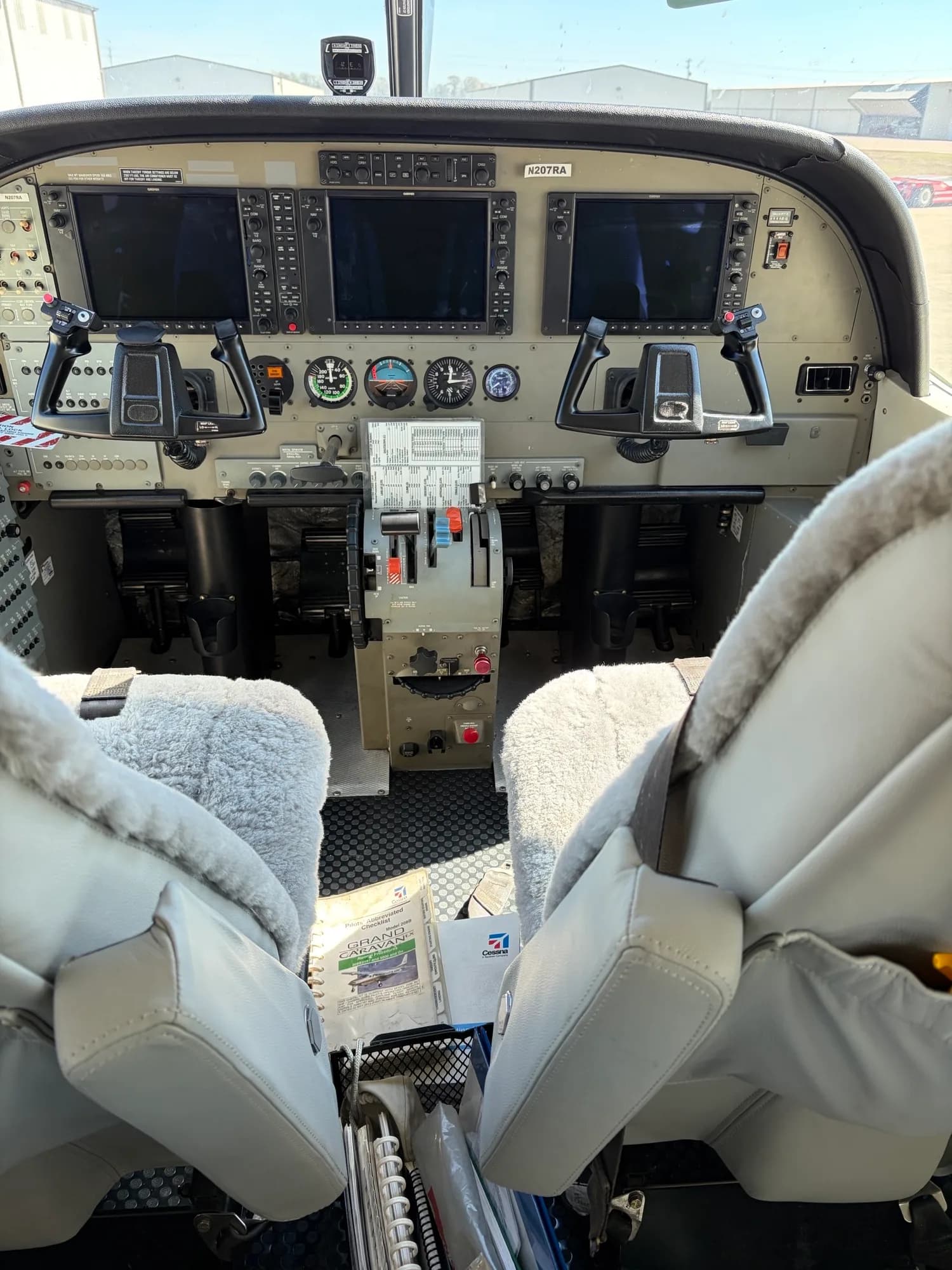 The cockpit of an aircraft features a dual-yoke control system, multiple screens, and various instruments.