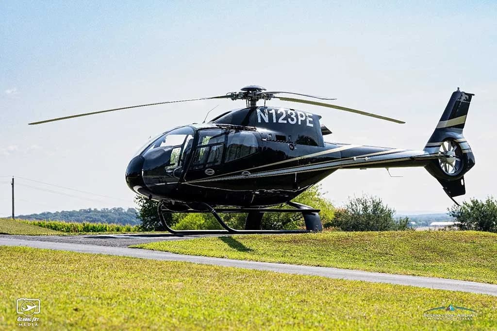 A black Eurocopter AS350 helicopter (N123PE) with silver stripes parked on a grassy area.