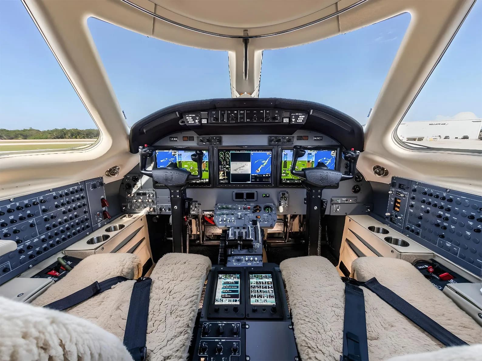 The cockpit of a private jet with multiple display screens and sheepskin seat covers.