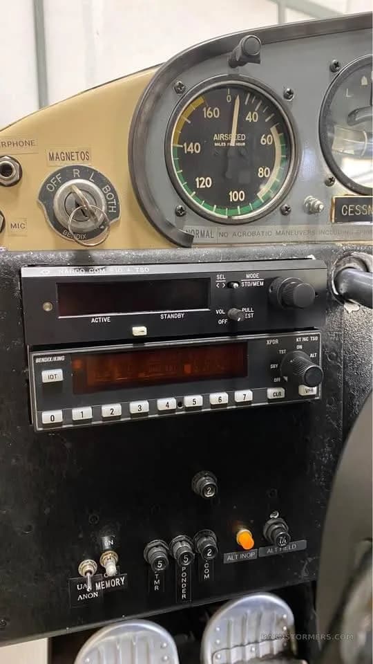 Close-up view of an aircraft's instrument panel, showing an airspeed indicator, radio stack, and ignition switch.