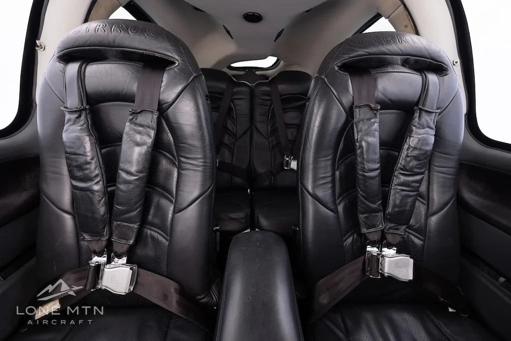 View of the black leather front and rear seats with seatbelts in the aircraft cabin.