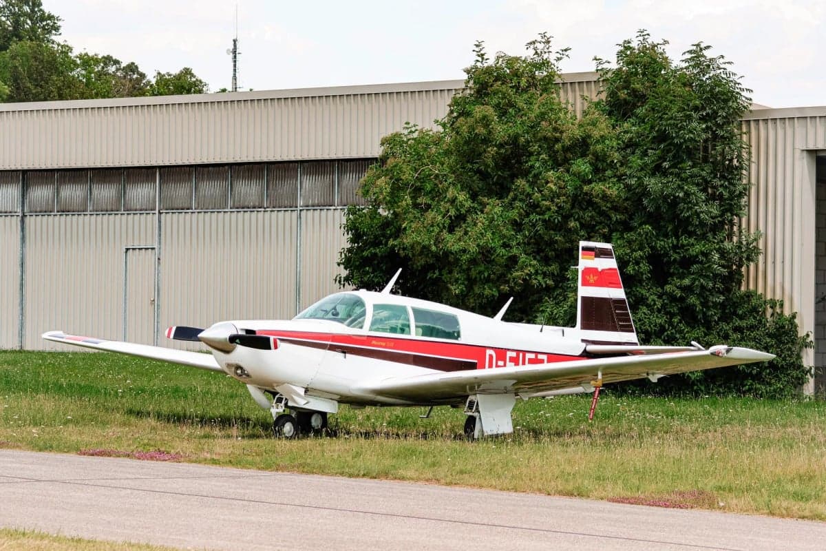 Mooney M20J aircraft D-EIFJ parked on the grass near a building.