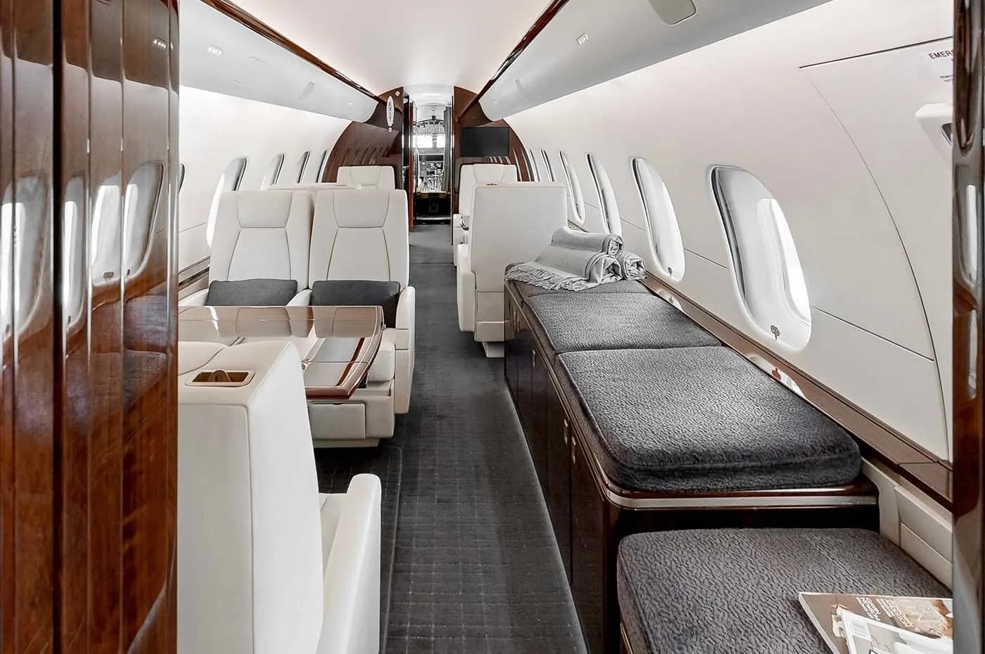 A long view of the business jet's cabin, featuring multiple cream seats, tables, and a lounge area with grey cushions.