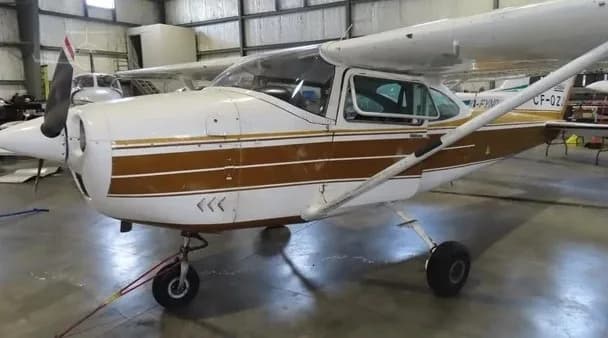 A white and brown single-engine high-wing aircraft, likely a Cessna, parked inside a hangar.