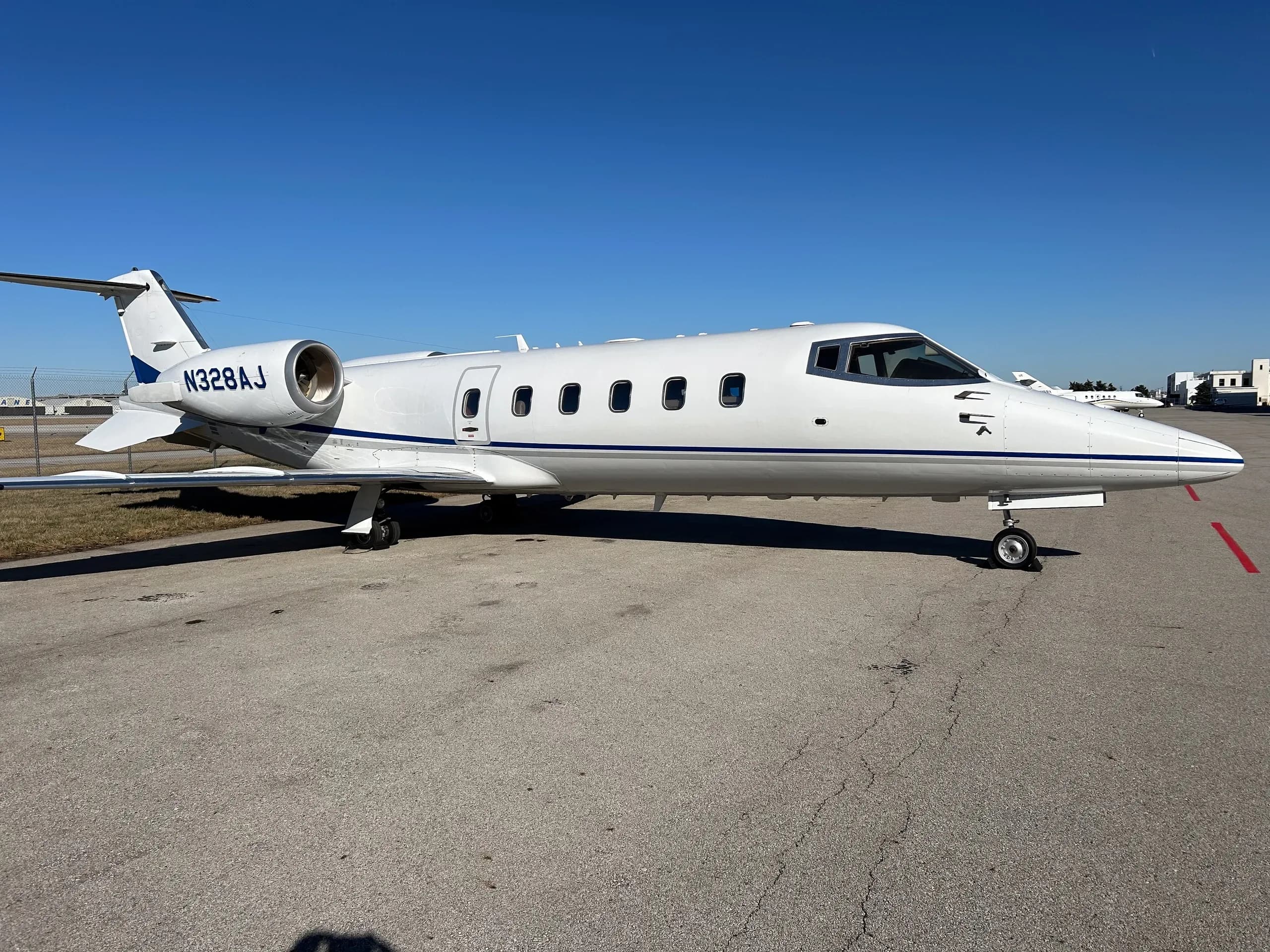 A thumbnail of the rear fuselage and tail of a white Learjet N328AJ with blue stripes.