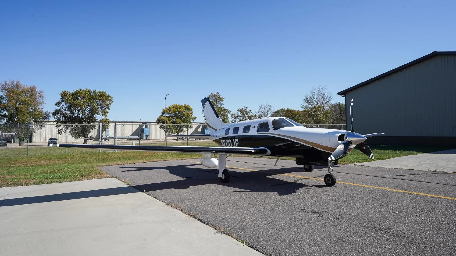 A front-side view of a white and black Piper Mirage N200JP with gold accents parked on an airfield.