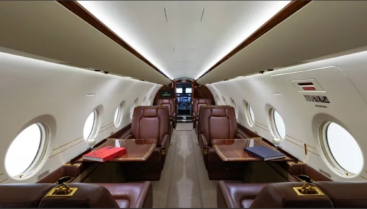 Cabin of a Gulfstream G280 with leather seats and wood tables, looking towards the cockpit.