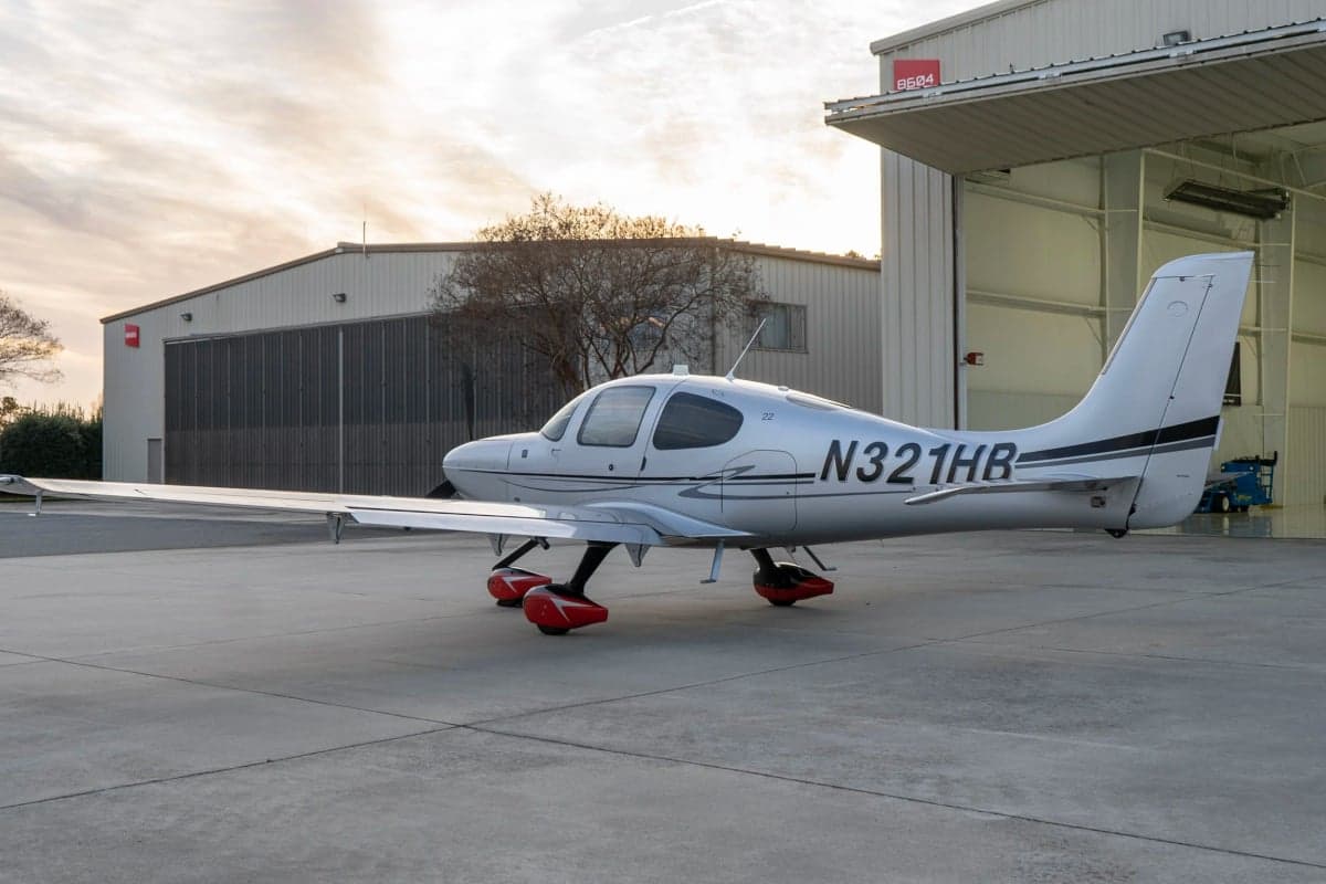A Cirrus SR22T aircraft with a silver paint scheme parked outside a hangar.