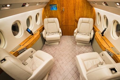 A private jet cabin section with four cream leather seats arranged around a central aisle.
