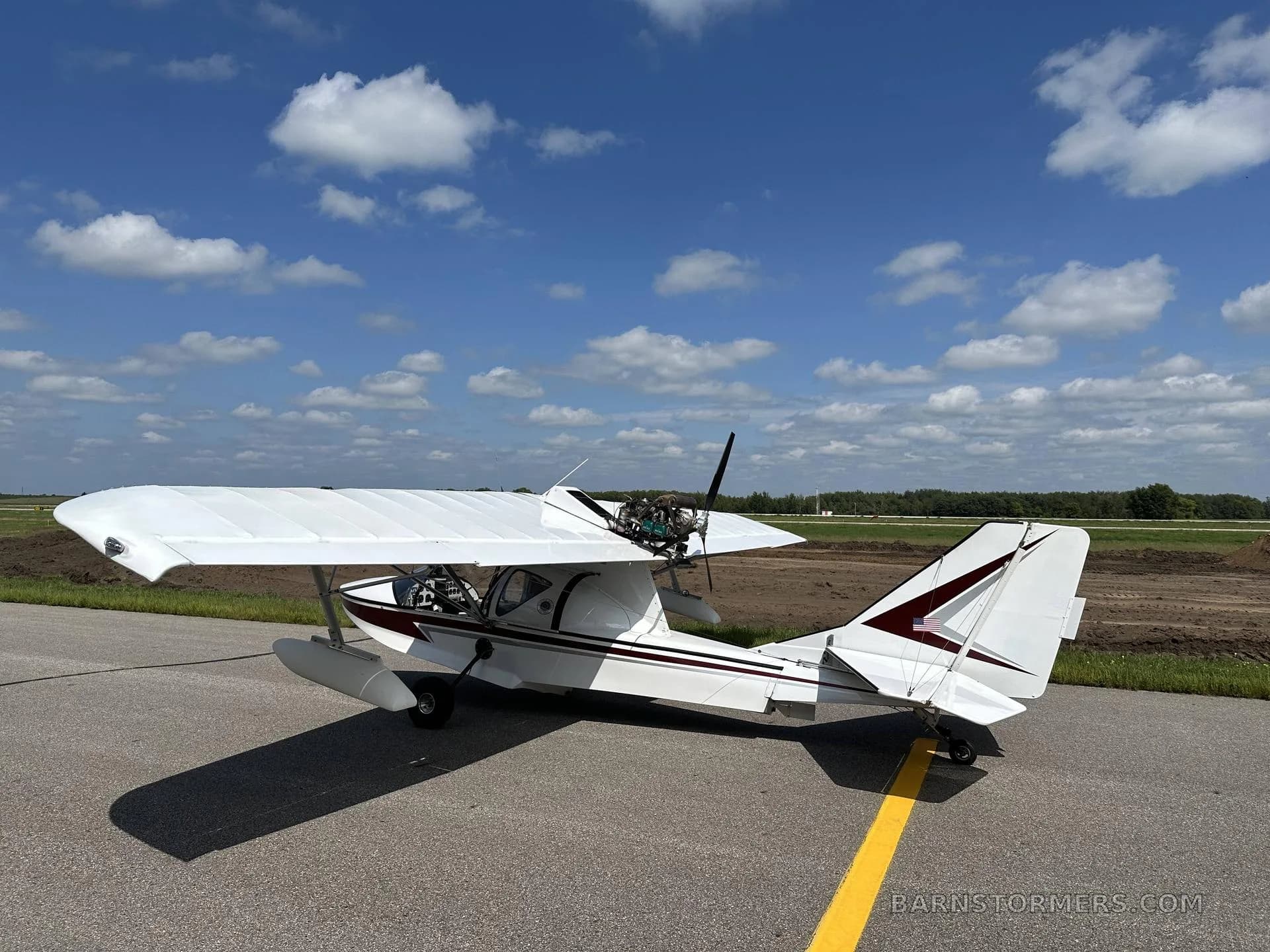A white and maroon Searey amphibian aircraft with registration N312AC is parked on an asphalt ramp, viewed from the rear-right, under a partly cloudy sky.