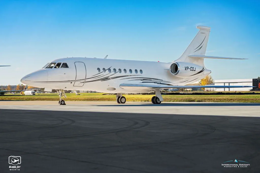 A white Dassault Falcon business jet with black and silver livery, registration VP-CDJ, parked on an tarmac.