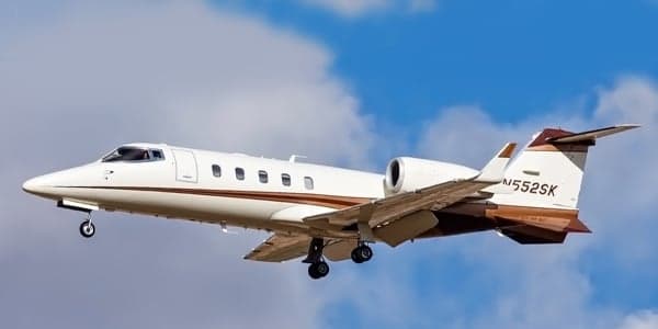 A white and brown Learjet is in flight against a blue sky.