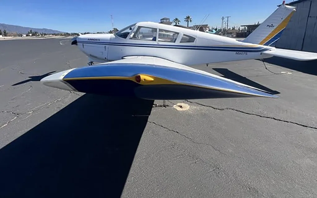 A white Piper Arrow II aircraft with blue and yellow stripes, registration N5107S, parked on an asphalt tarmac.