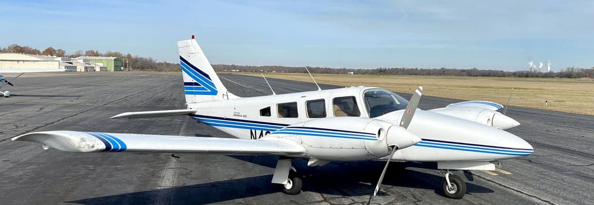 A Piper Aztec aircraft is parked on the tarmac with a white and blue paint scheme.