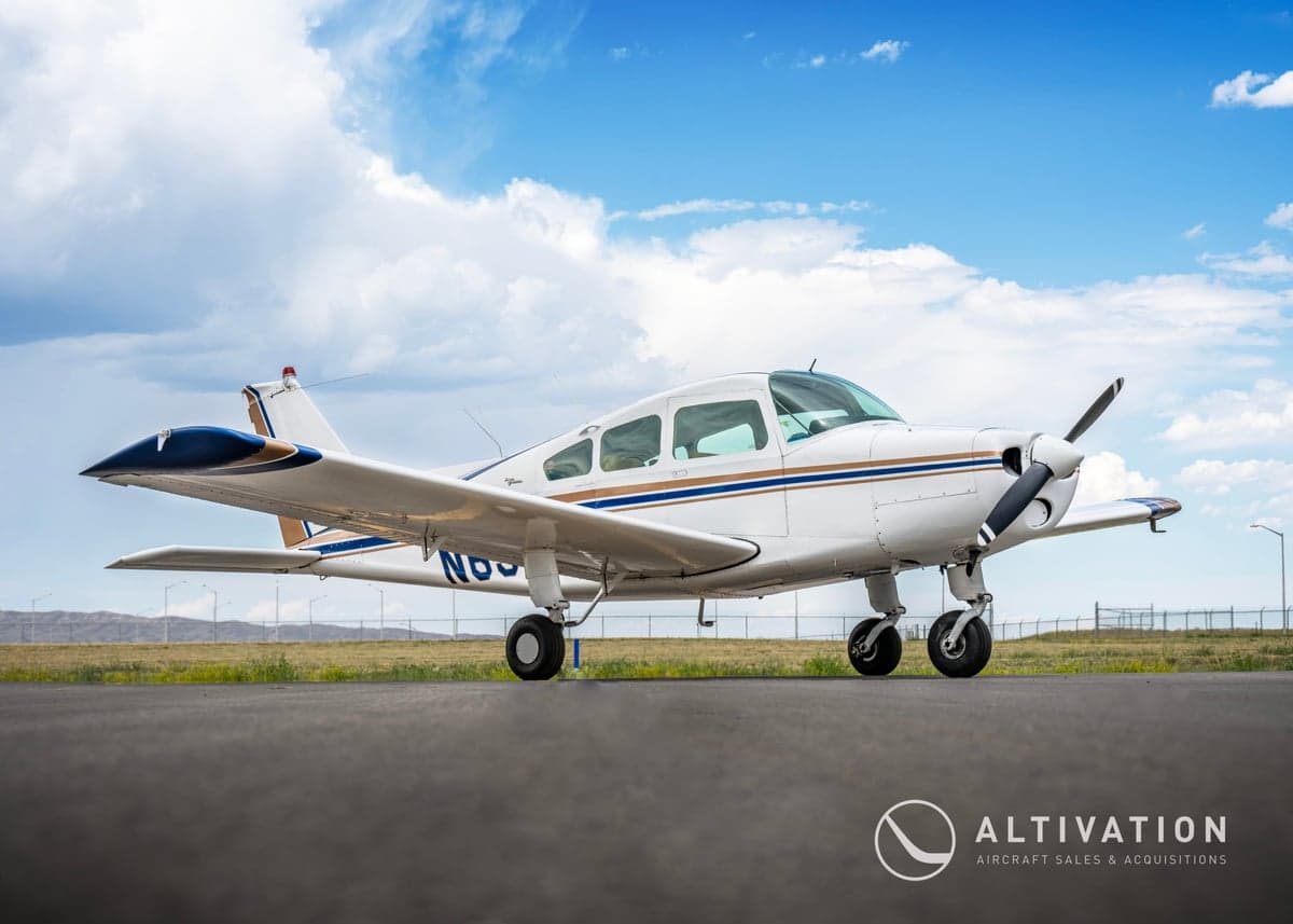 A white and blue Piper aircraft is parked on the tarmac on a sunny day.