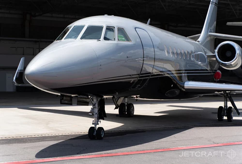 A close-up front-left view of a silver and black business jet parked on an airport tarmac.