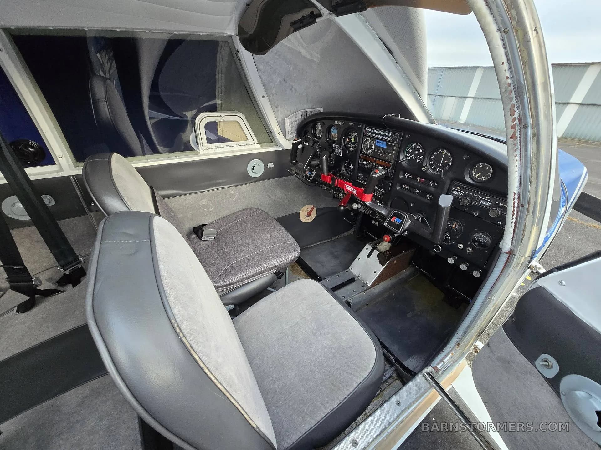 The cockpit interior of a small aircraft showing grey seats, control yokes, and the instrument panel.