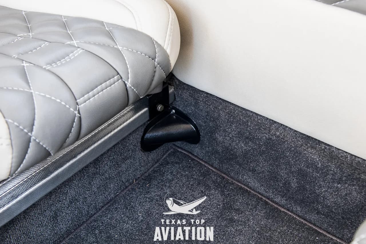 A close-up of the seat rail and dark grey carpeted floor in the aircraft's interior.