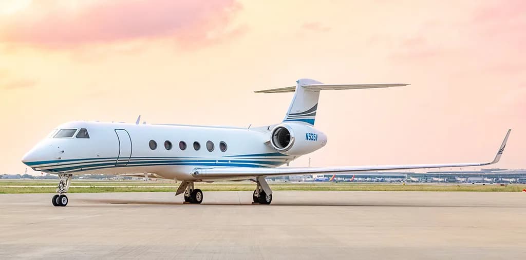 A Gulfstream G550 business jet with a white and blue livery, tail number N535V, parked on the tarmac at sunset.