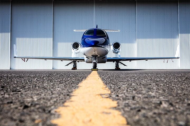Front view of a HondaJet parked on the tarmac in front of a hangar.