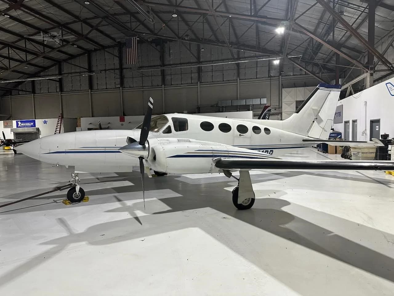 A white Cessna 414 Chancellor twin-engine aircraft with blue stripes is parked inside a hangar.