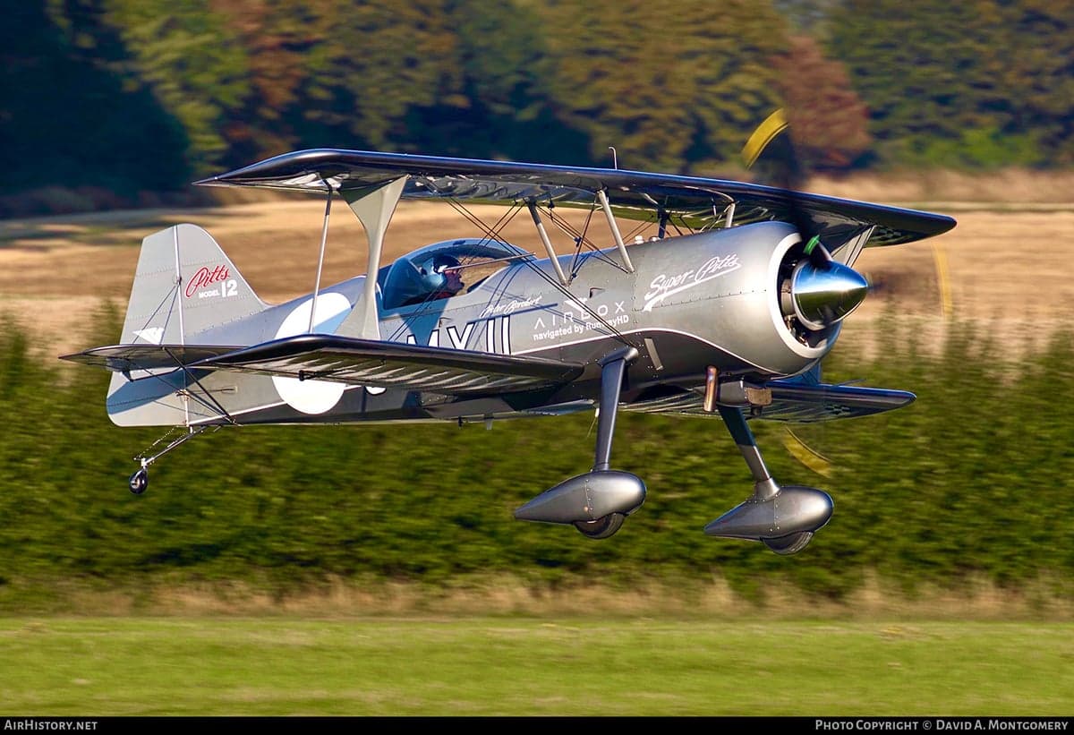A silver and black Pitts Model 12 biplane in flight.