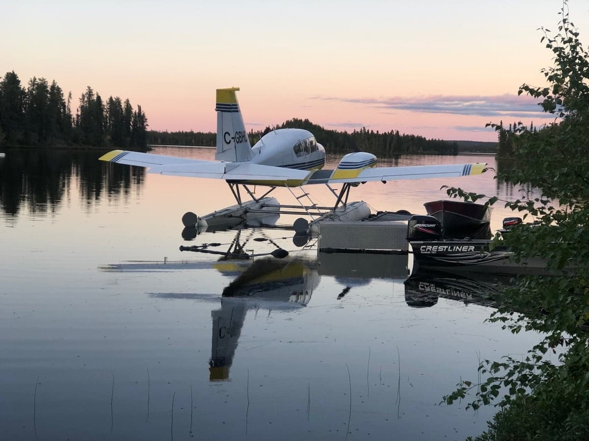 Yellow and white twin engine aircraft on floats, on a trailer near a lake.