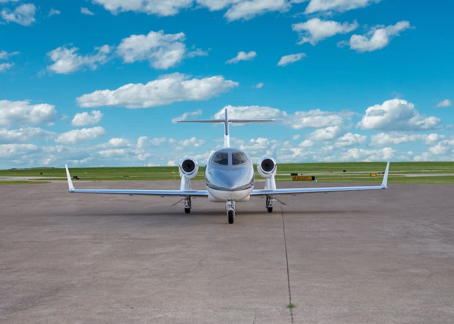 A white and grey HondaJet is parked on a concrete tarmac, viewed from the front.