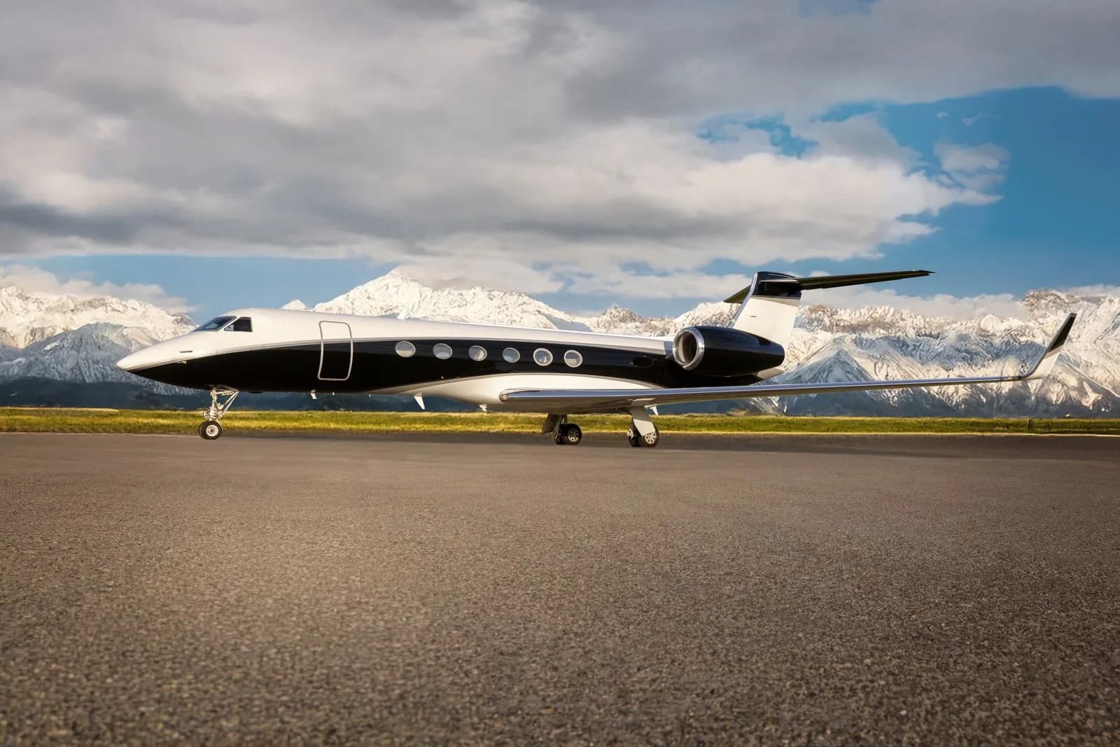 A black and white Gulfstream jet parked on the tarmac with snow-capped mountains in the background.