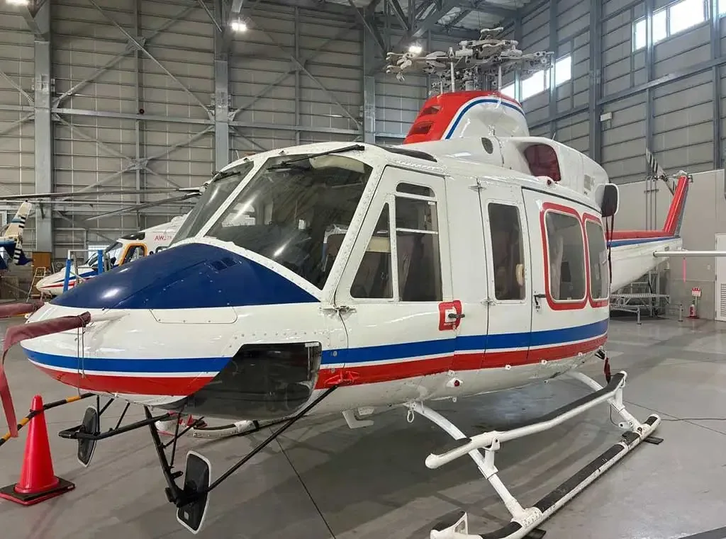 A white helicopter with blue and red stripes on its nose and tail, parked in a hangar.
