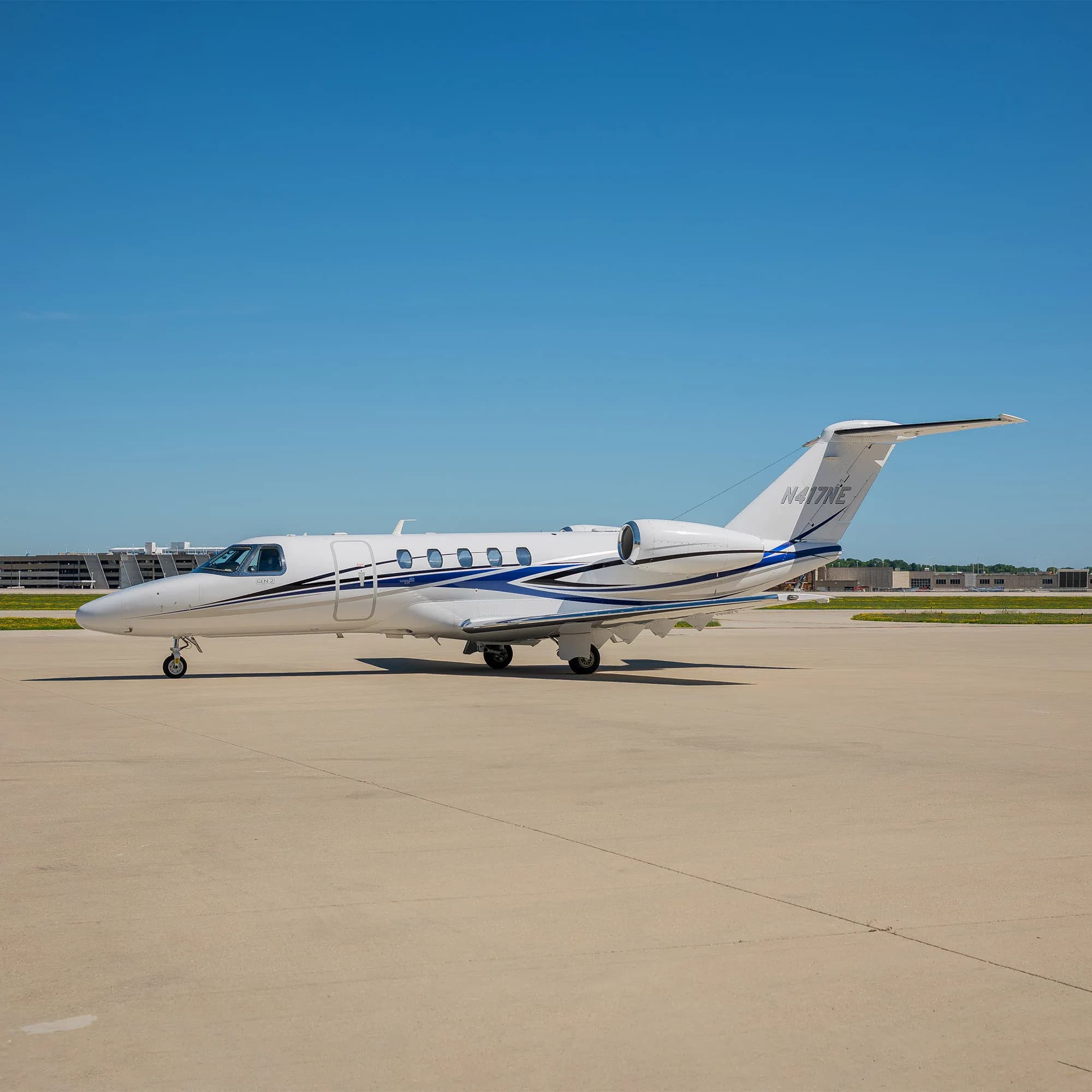 A white business jet with blue and grey stripes on an airfield under a clear blue sky.